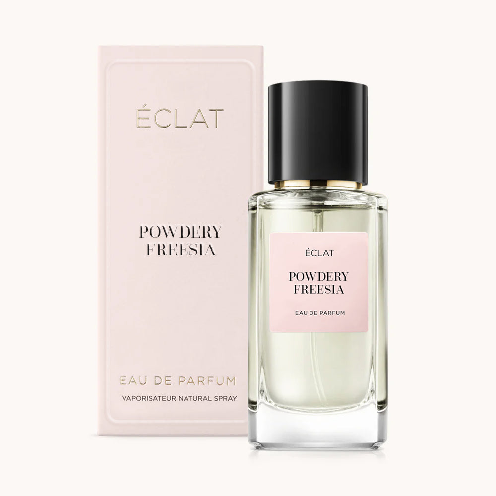 ÉCLAT Powdery Freesia women’s perfume bottle with matching light pink packaging. The elegant flacon features a black cylindrical magnetic cap and a light pink label with the inscription ÉCLAT Powdery Freesia and “Eau de Parfum”.