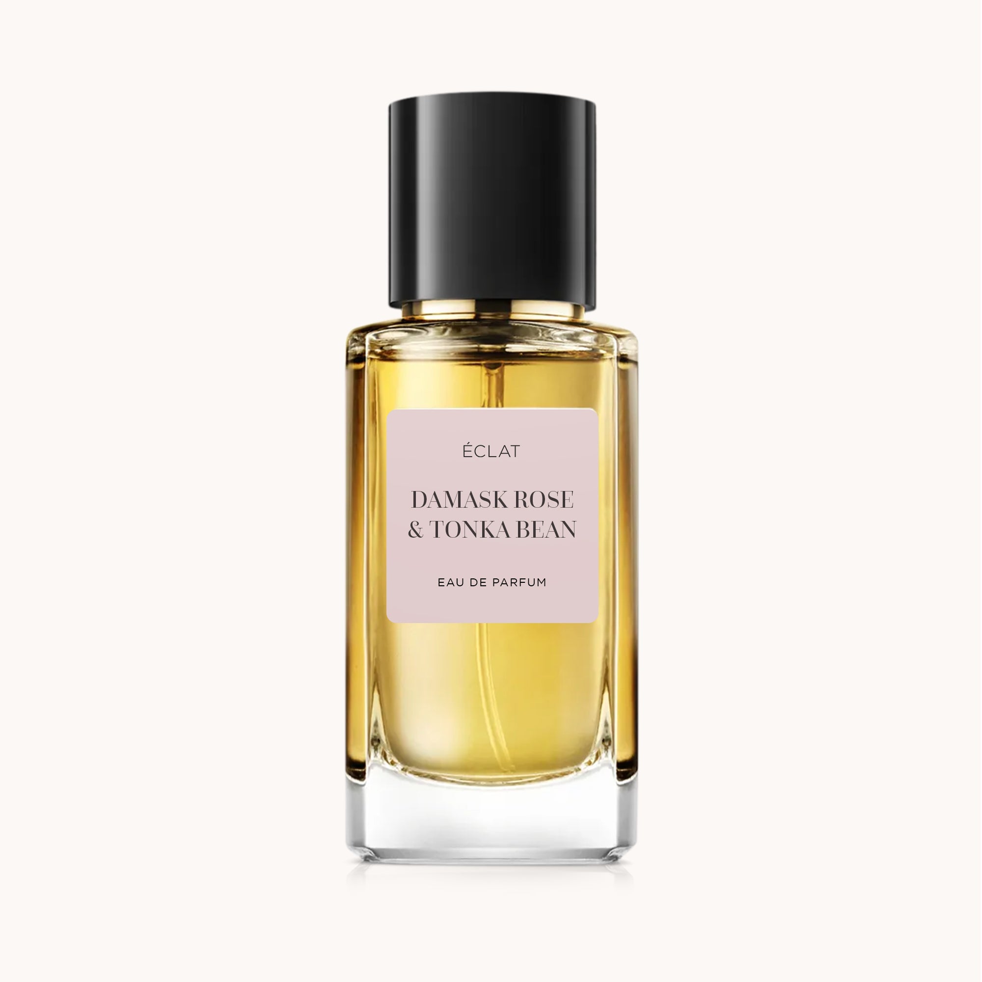 Faceted glass bottle with a golden hue and a matte black cap, featuring a pink label of ÉCLAT Damask Rose & Tonka Bean.
