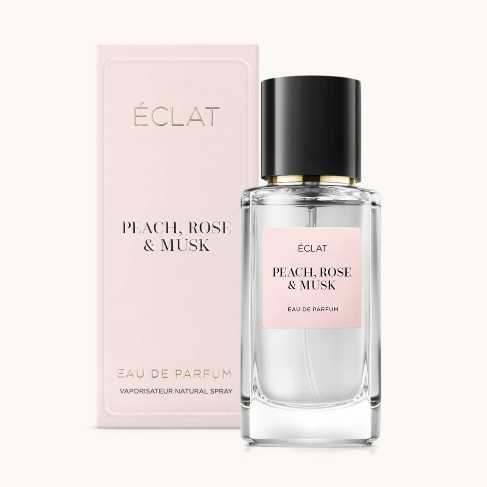 ÉCLAT Peach, Rose & Musk perfume bottle with a clear glass flacon and black cap, accompanied by a pale pink box.