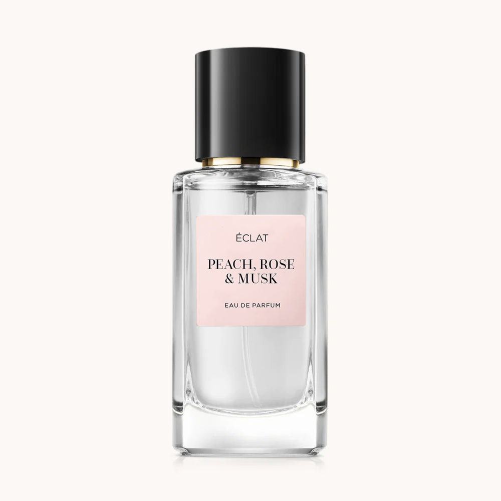 Faceted glass bottle of ÉCLAT Peach, Rose & Musk with a matte pink label and a glossy black cap.