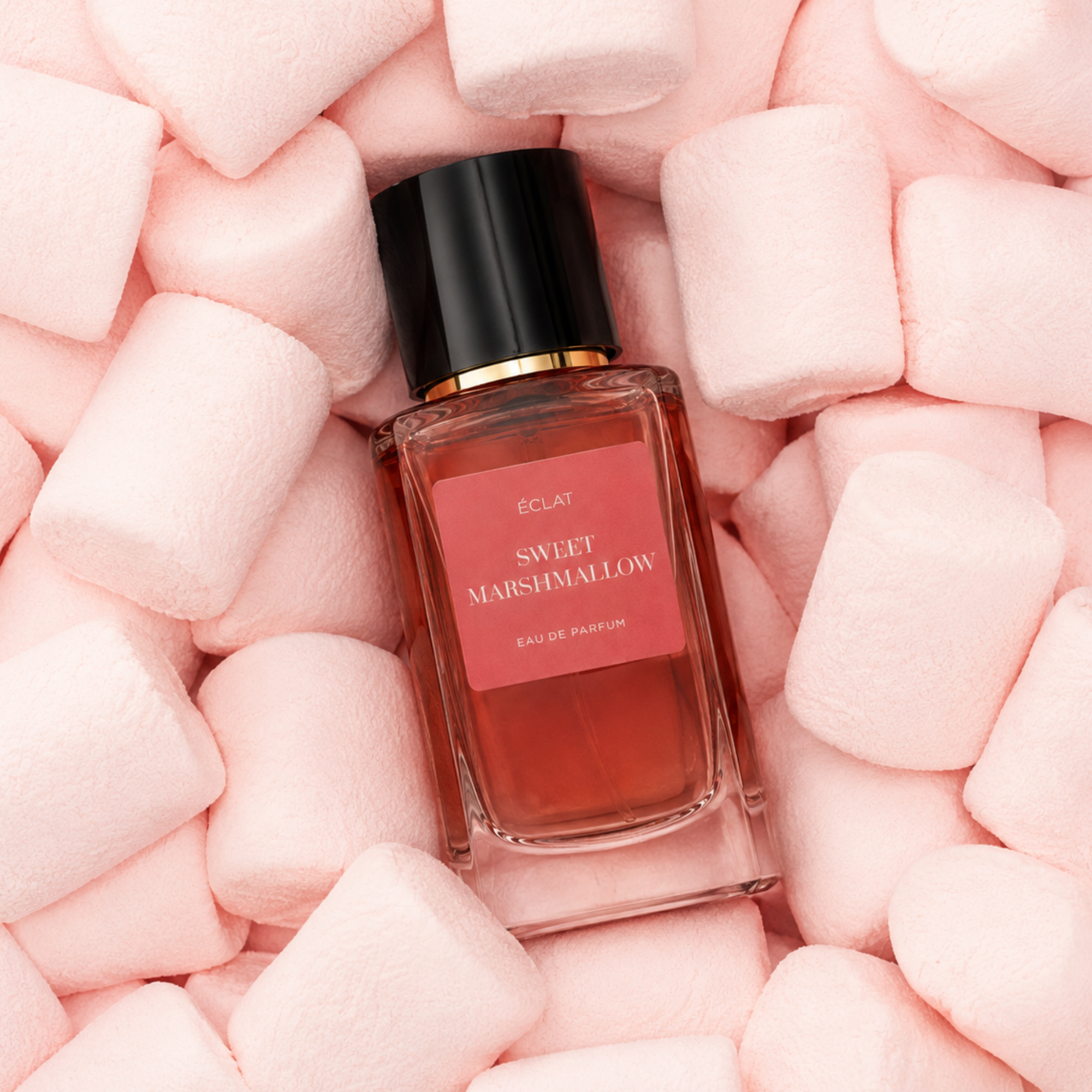 A glass bottle of ÉCLAT Sweet Marshmallow surrounded by soft pink marshmallows, featuring a black cap and a pink label.