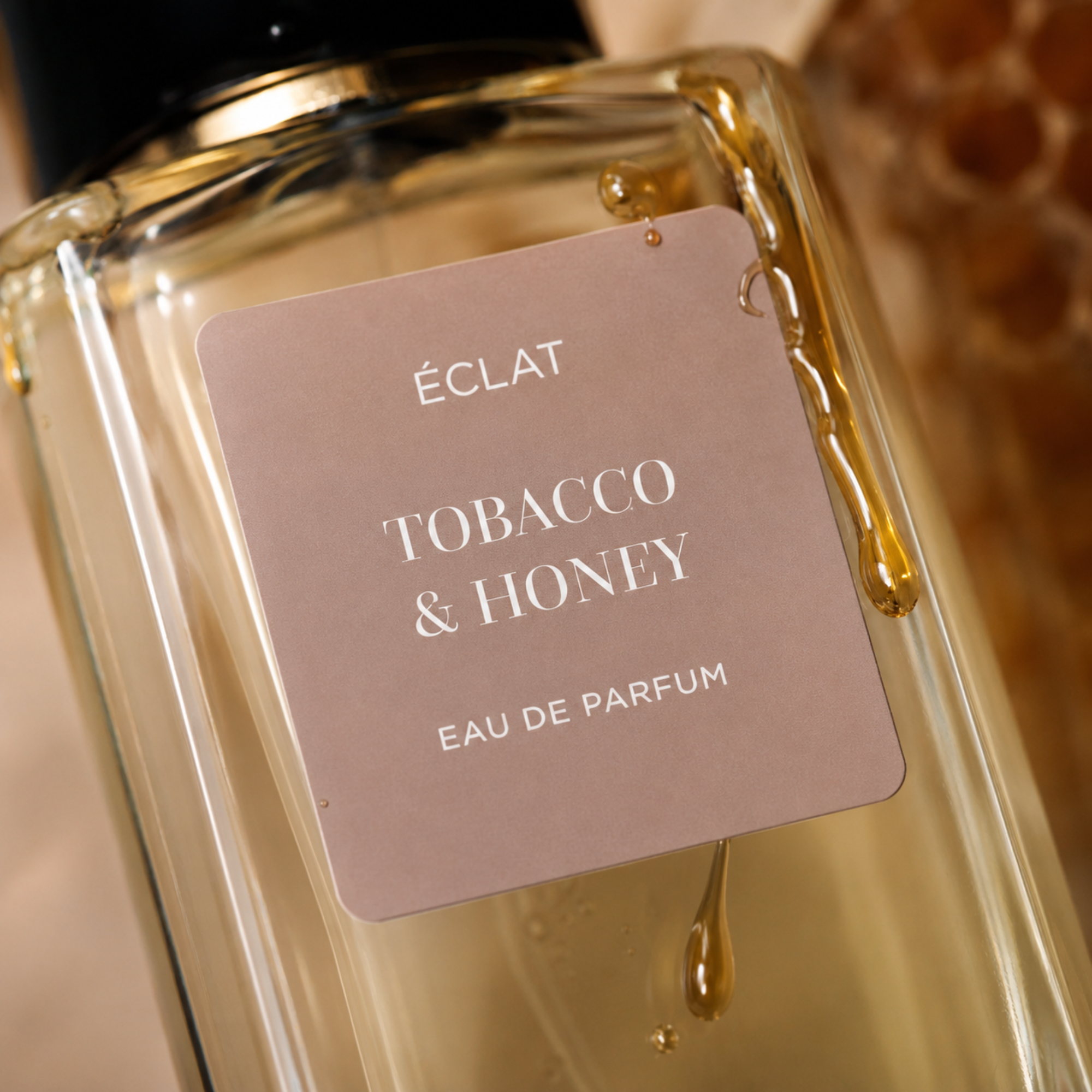 ÉCLAT Tobacco & Honey perfume bottle with a light brown matte label and a honey drop flowing over the glass surface.