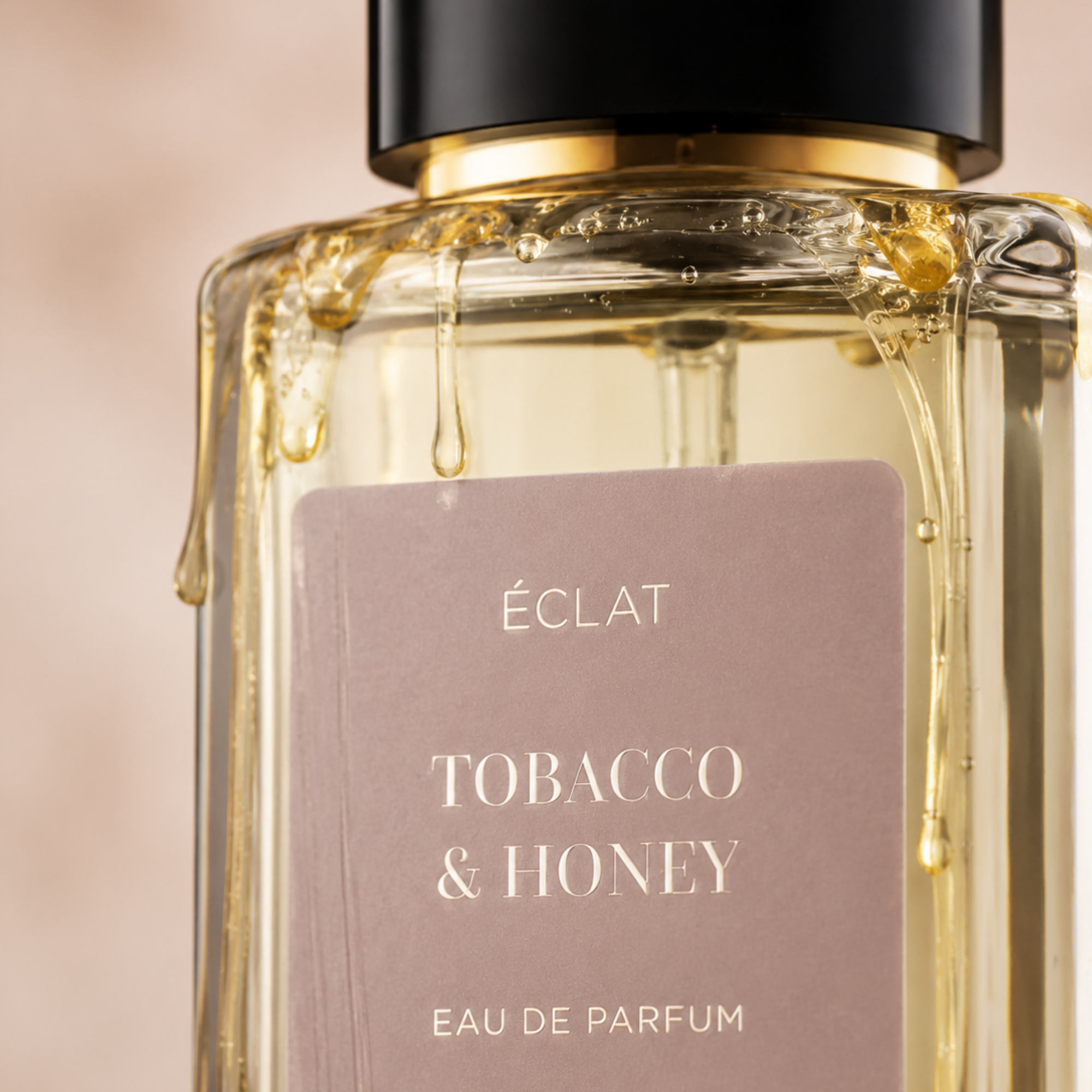 A faceted glass bottle of ÉCLAT Tobacco & Honey with a satin finish label and a black cap, decorated with honey drips.