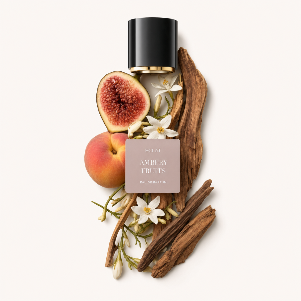 Une composition de figue coupée, pêche entière, fleurs blanches et éléments en bois entoure l'étiquette ÉCLAT Ambery Fruits sous un capuchon noir à intérieur doré.