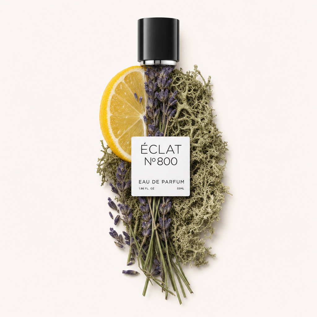 An arrangement of a lemon slice, sprigs of lavender, and oak moss surround the original black cap with ÉCLAT Aromatic Oak Moss label.