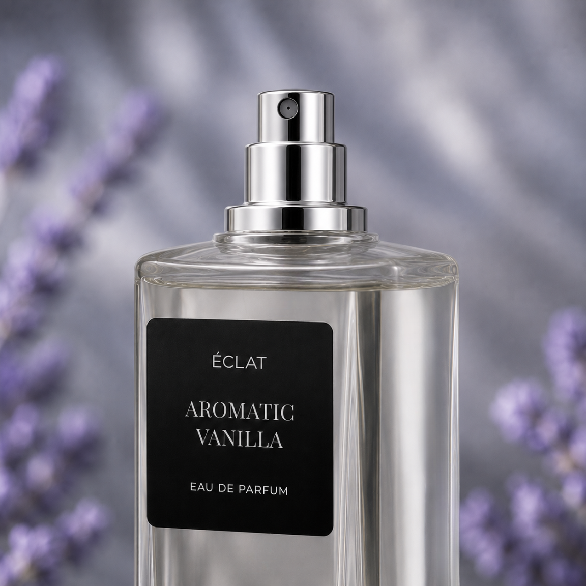 A clear glass bottle of ÉCLAT Aromatic Vanilla with a polished silver spray cap and a black matte label, set against a blurred lavender background.