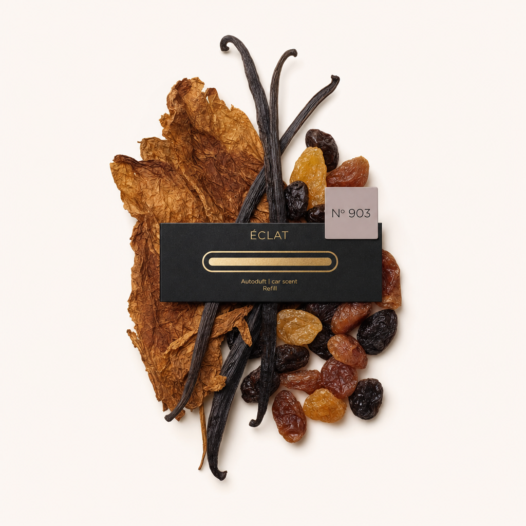 Een arrangement van gedroogde tabaksbladeren, vanillepeulen en diverse rozijnen omringt een zwarte ÉCLAT-dop met label nr. 903.