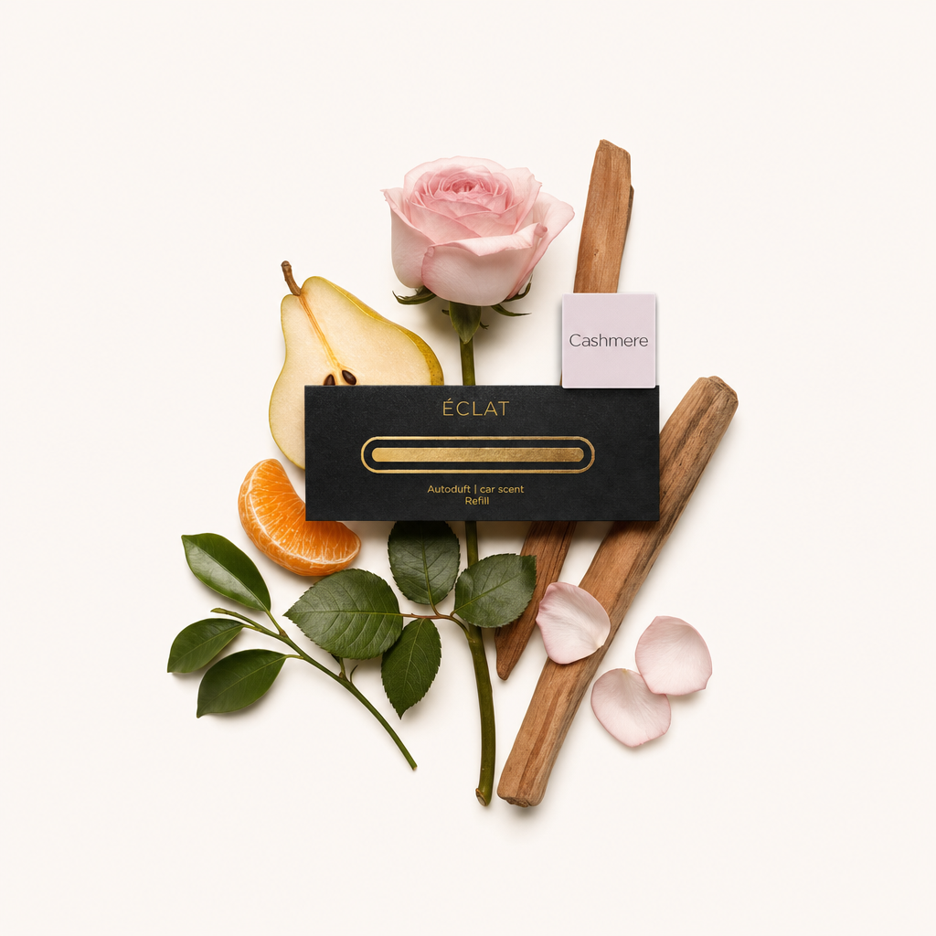 Un arrangement délicat avec une rose rose pâle, une poire tranchée, un segment de mandarine, deux bâtons en bois, des feuilles vertes et des pétales épars, à côté du capuchon noir d'ÉCLAT avec une étiquette 'Cashmere'.