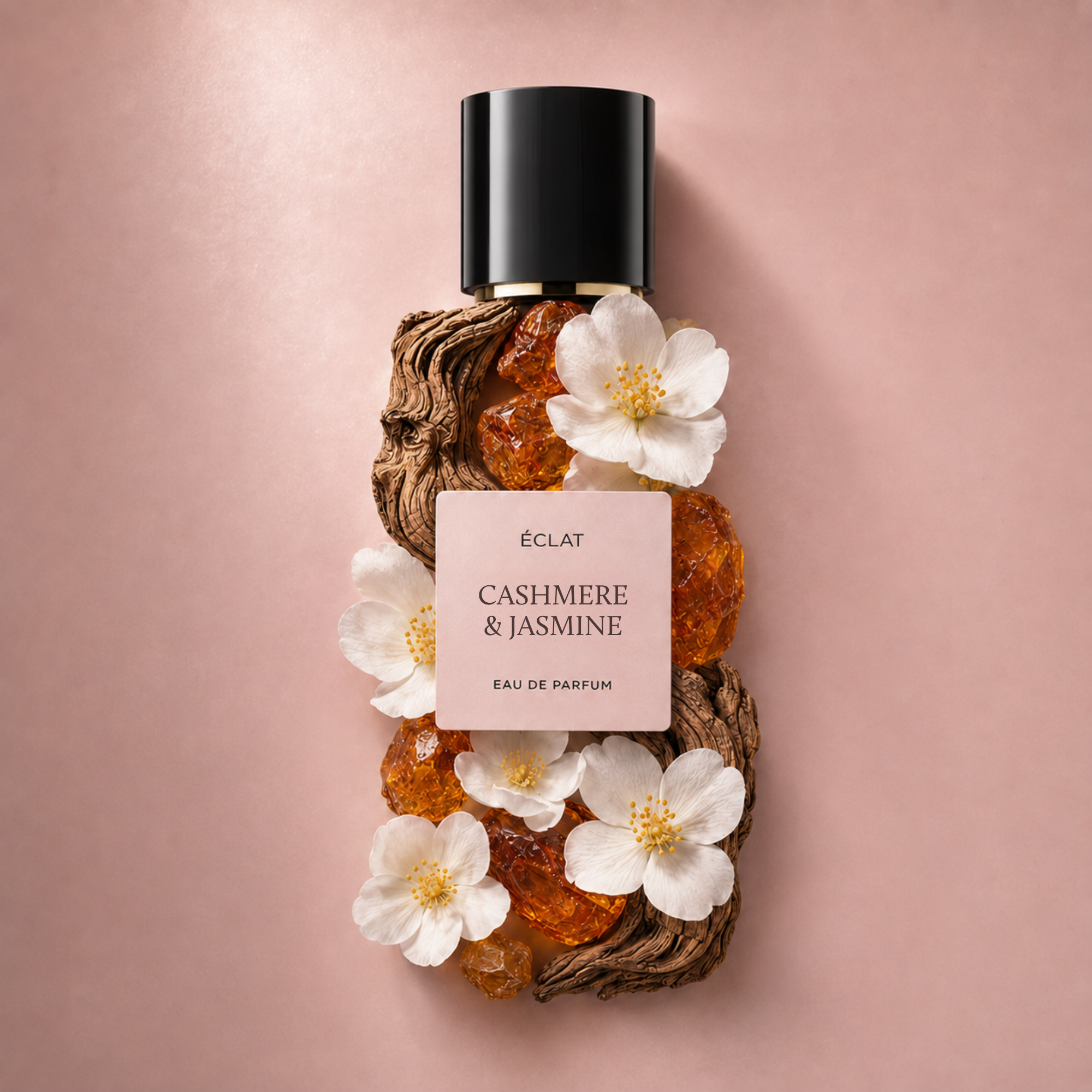 ÉCLAT Cashmere & Jasmine perfume bottle adorned with white flowers and amber crystals against a pink background.