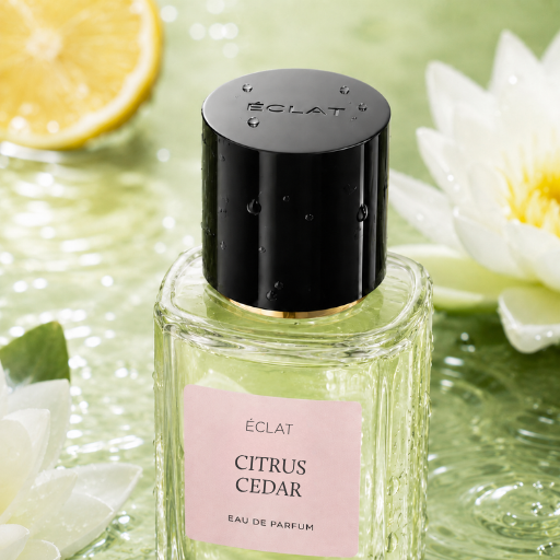 Faceted glass bottle of ÉCLAT Citrus Cedar with a black cap on a water surface with lemon slice and white flowers.