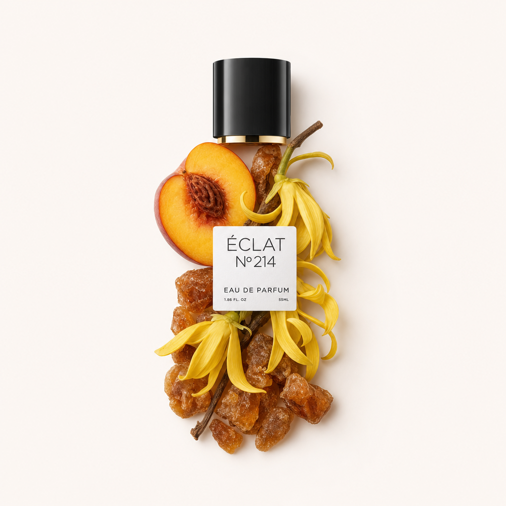 Un arrangement de fleurs d'ylang-ylang jaunes, de résine d'ambre et d'une demi-pêche autour d'un bouchon noir avec une étiquette pour ÉCLAT Creamy Amber.