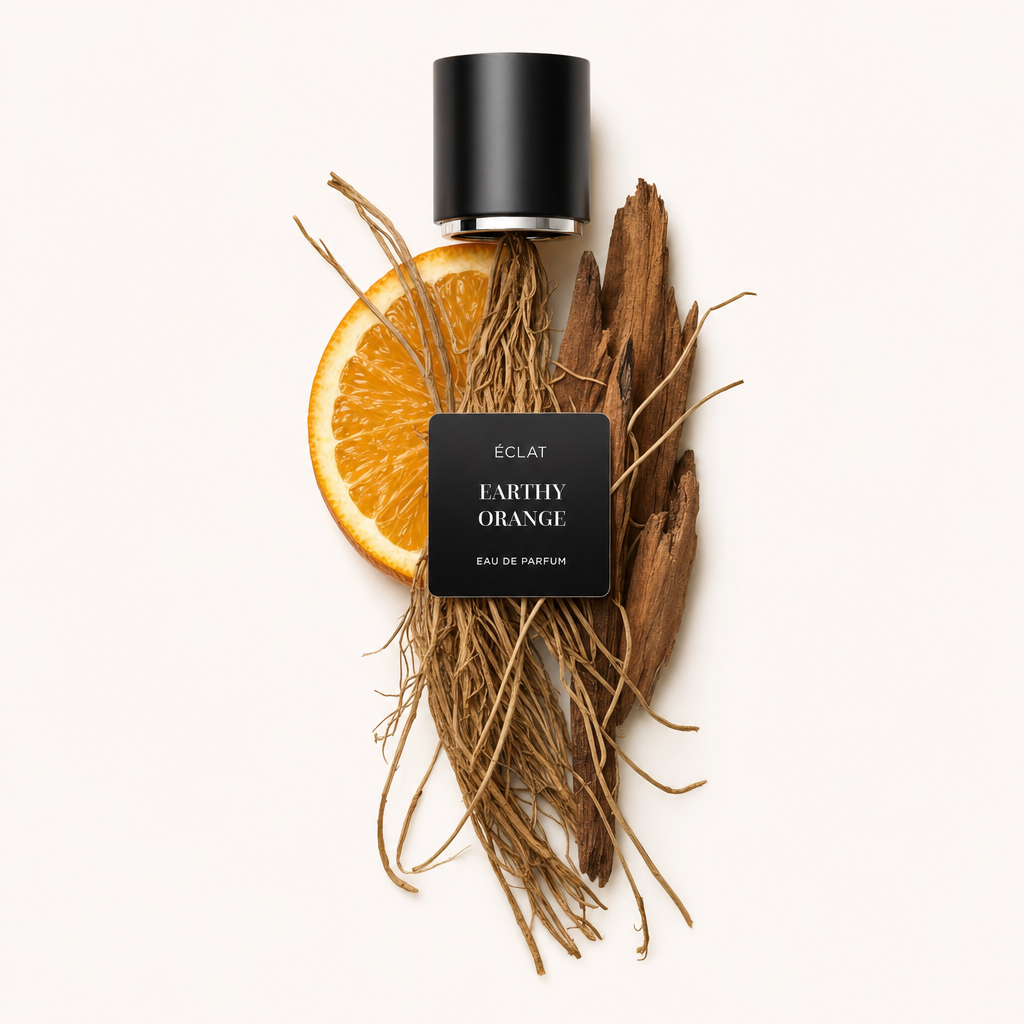 Un arrangement de racines terreuses, une tranche d'orange et des morceaux de bois sous un capuchon noir avec étiquette ÉCLAT Earthy Orange.