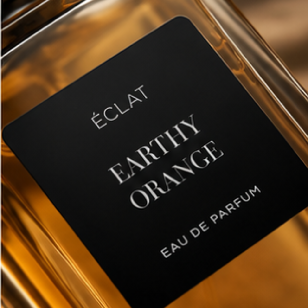 A glass flacon with a warm amber hue, featuring a black matte label with the inscription ÉCLAT Earthy Orange.