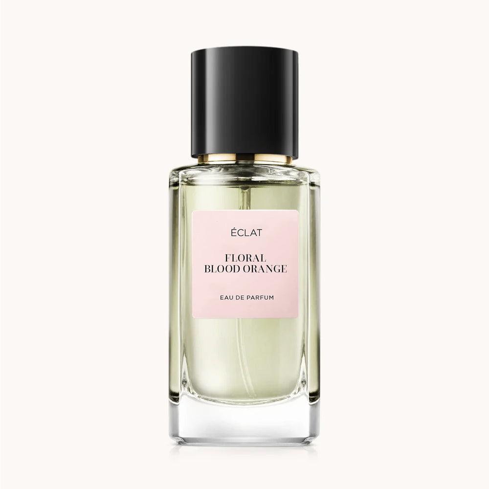 Un frasco de vidrio facetado con tapa negra y etiqueta rosa para el perfume ÉCLAT Floral Blood Orange.