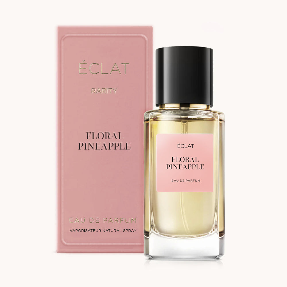 Un frasco de vidrio facetado de ÉCLAT Floral Pineapple con tapa negra, acompañado de una caja rosa con el mismo nombre.
