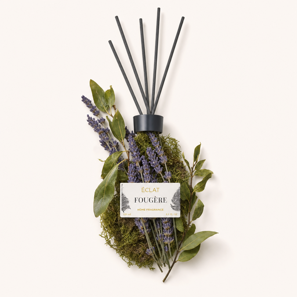 Een arrangement met lavendelsprietjes en groene bladeren rondom een zwarte dop met etiket, die de ÉCLAT Fougère Room Fragrance benadrukt.