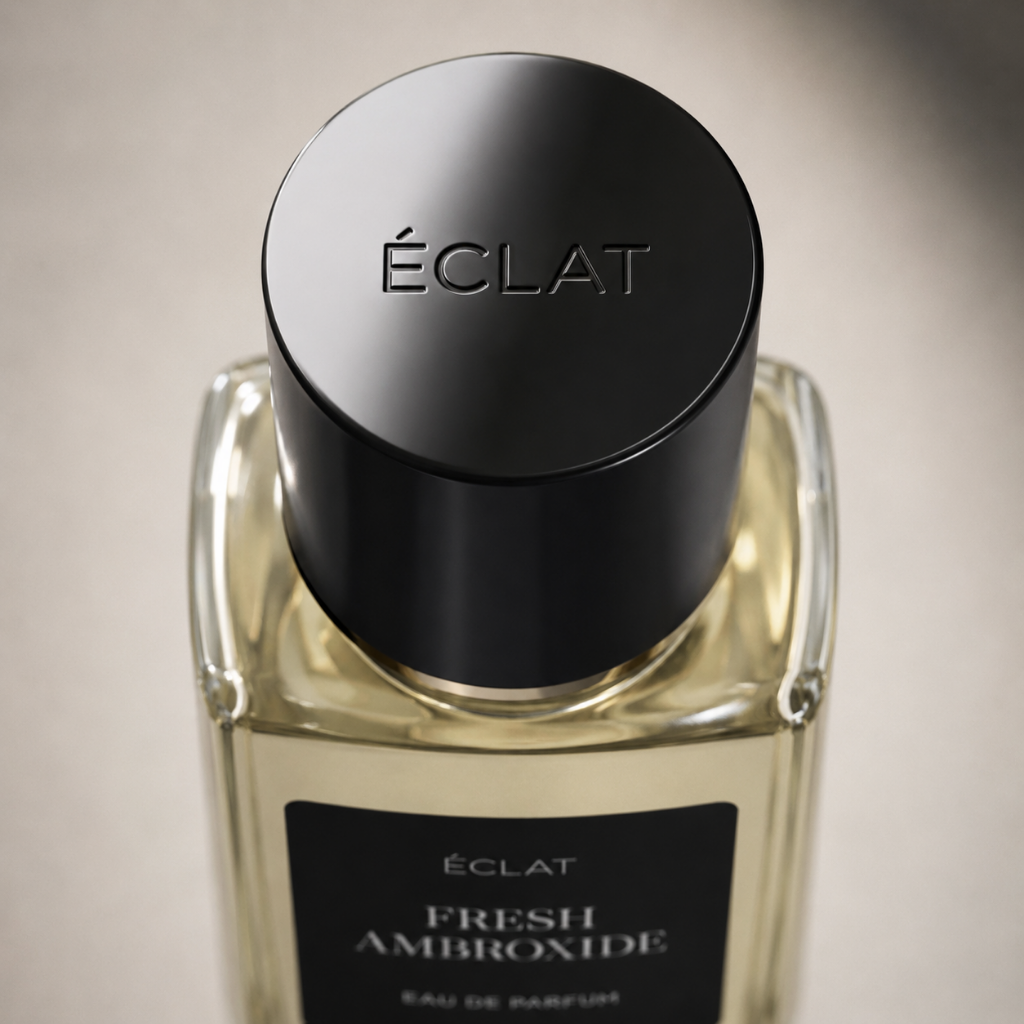 A faceted glass flacon of ÉCLAT Fresh Ambroxide with a sleek black cap and a matte label against a neutral background.