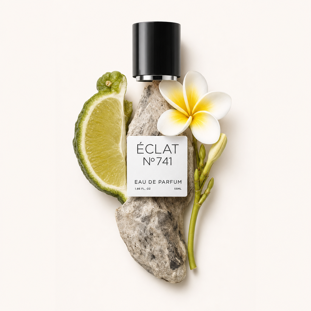 Un capuchon noir avec étiquette est entouré de cardamome fraîche, d'une tranche de citron vert et d'un frangipanier blanc sur un morceau de bois flotté clair.