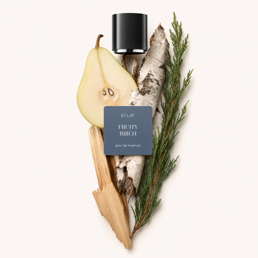 An artful arrangement featuring a sliced pear, birch bark, and cypress sprigs, crowned by a black cap labeled ÉCLAT Fruity Birch.