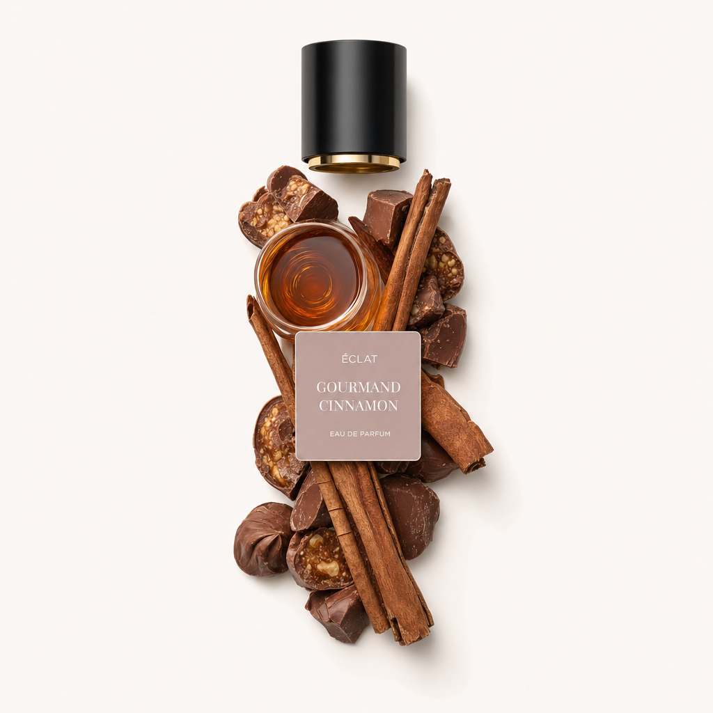 A carefully arranged still life of ÉCLAT Gourmand Cinnamon features cinnamon sticks, chocolate pieces, and nuts surrounding a small glass dish of liquid. The composition is crowned with a black cap featuring a label.