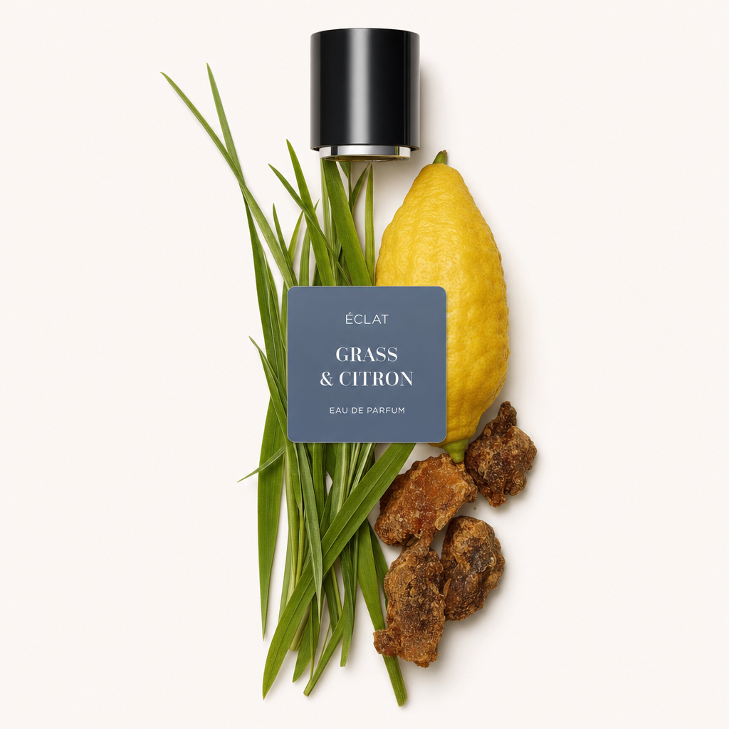 Un arrangement de brins d'herbe, un cédrat entier et des morceaux de résine est présenté avec un capuchon noir portant une étiquette d'ÉCLAT Grass & Citron.