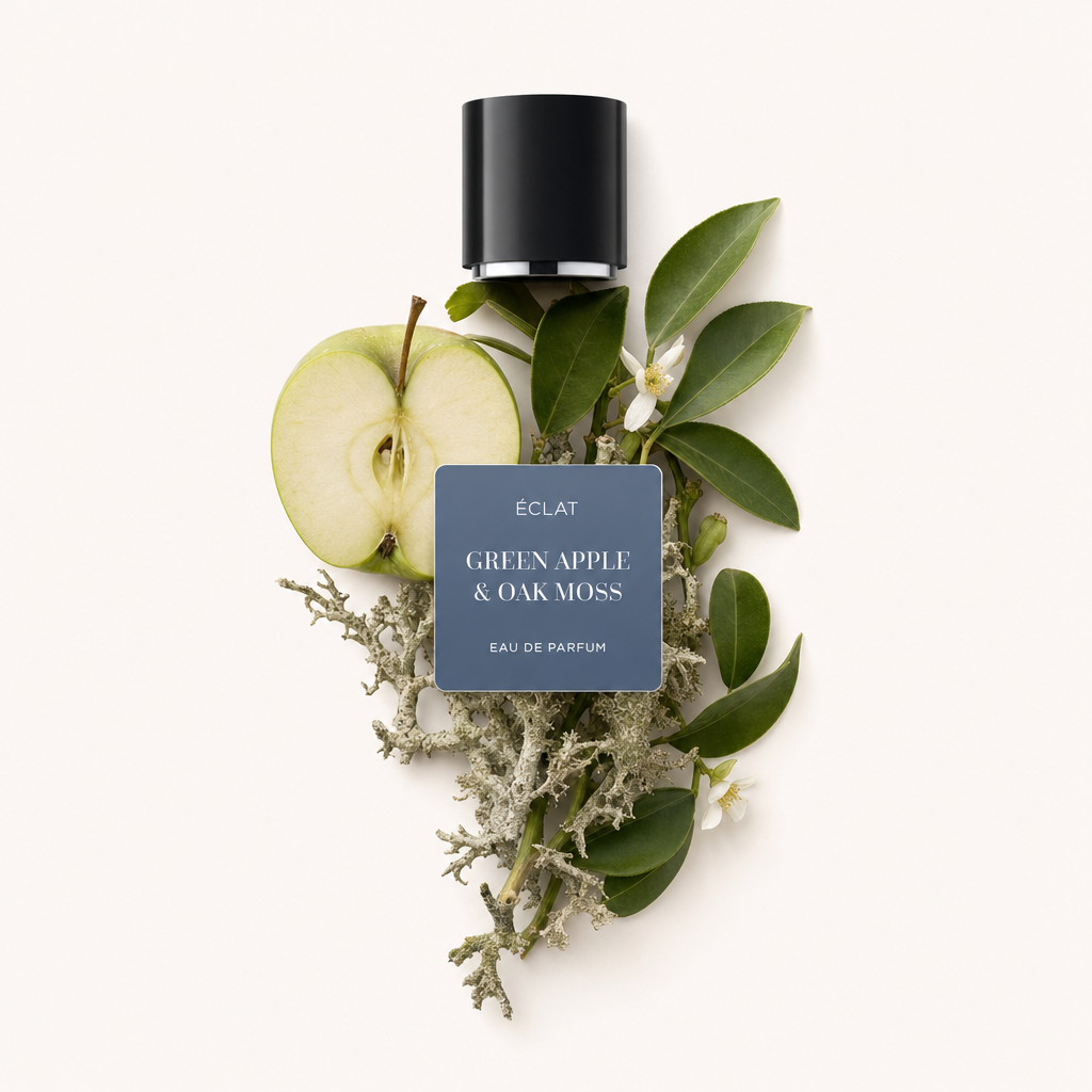 Un agencement de moitié de pomme verte, mousse de chêne et feuillage luxuriant repose sous un bouchon noir avec une étiquette présentant ÉCLAT Green Apple & Oak Moss.