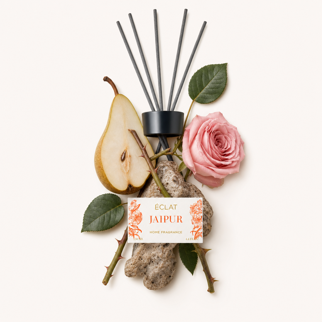 Um arranjo de notas de fragrância ÉCLAT Jaipur com uma rosa, fatia de pêra, folhas verdes e pedras texturizadas, junto a uma tampa preta com etiqueta.
