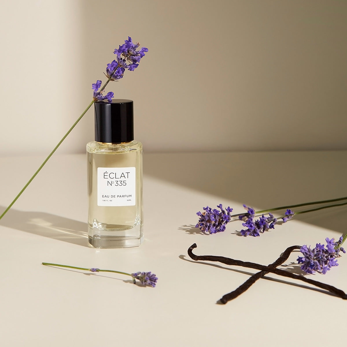 Flacon en verre facetté ÉCLAT Lavender & Vanilla avec bouchon noir, entouré de brins de lavande et de gousses de vanille.