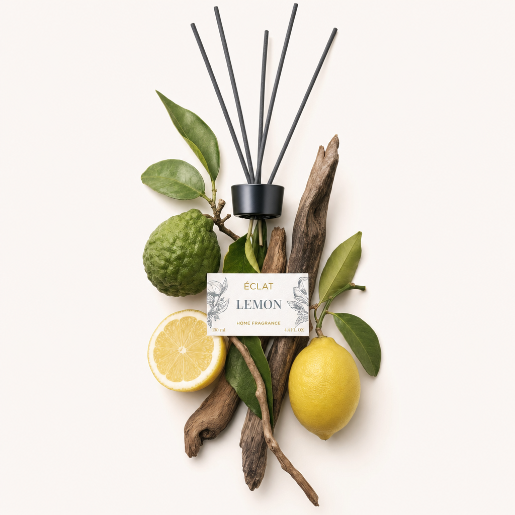 Een compositie van ingrediënten met citroen, bergamot en houtstukken rond een zwarte dop met stokjes en een label voor ÉCLAT Lemon Room Fragrance Sticks.