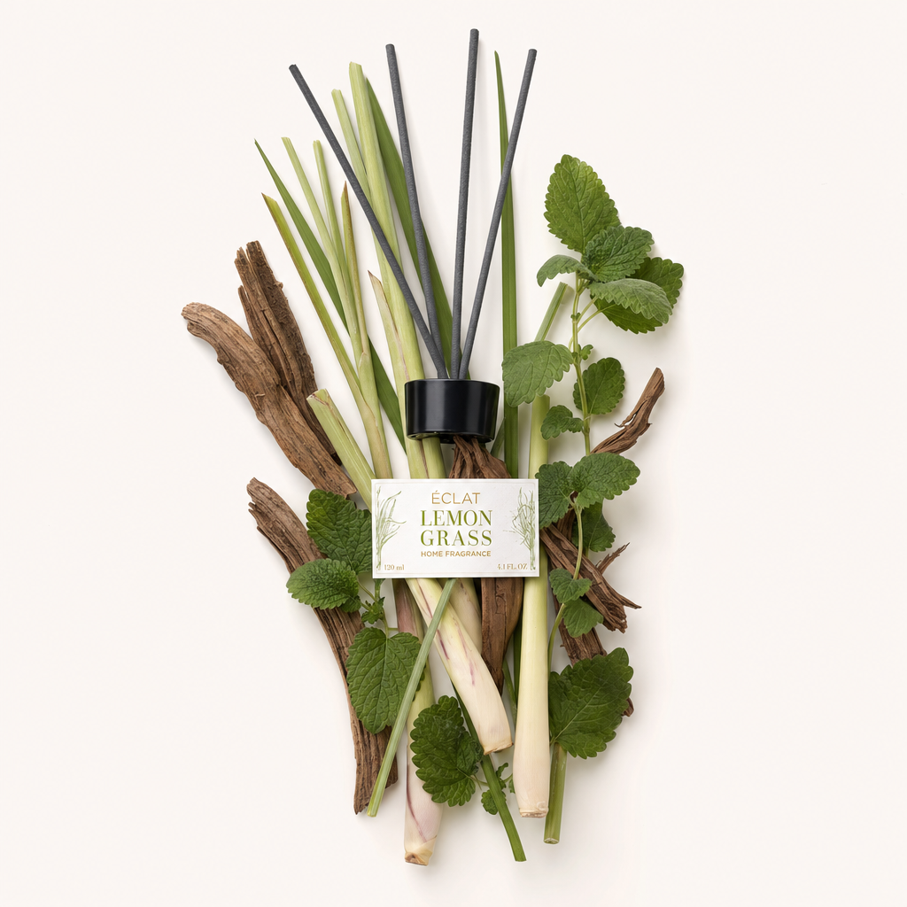 Ett arrangemang av citrongräs, myntablad och träbitar omger den svarta kapsylen med ÉCLAT Lemongrass Room Fragrance Sticks etikett.