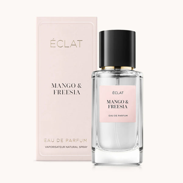 Perfume ÉCLAT Mango & Freesia en frasco de vidrio transparente con tapa negra, acompañado de una caja de embalaje rosa suave.