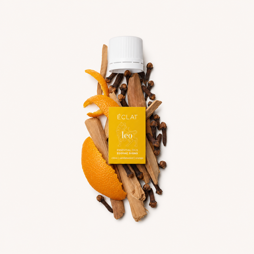 Un arrangement d'écorce d'orange, de bâtons de santal et de clous de girofle entoure un bouchon blanc avec une étiquette jaune de 'Natural Oil Blend - Zodiac Sign Leo' d'ÉCLAT.