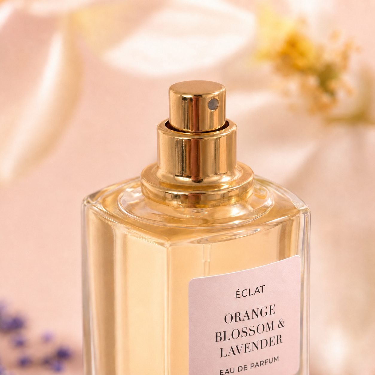 Faceted glass bottle of ÉCLAT Orange Blossom & Lavender with a gold-colored spray nozzle against a soft floral background.