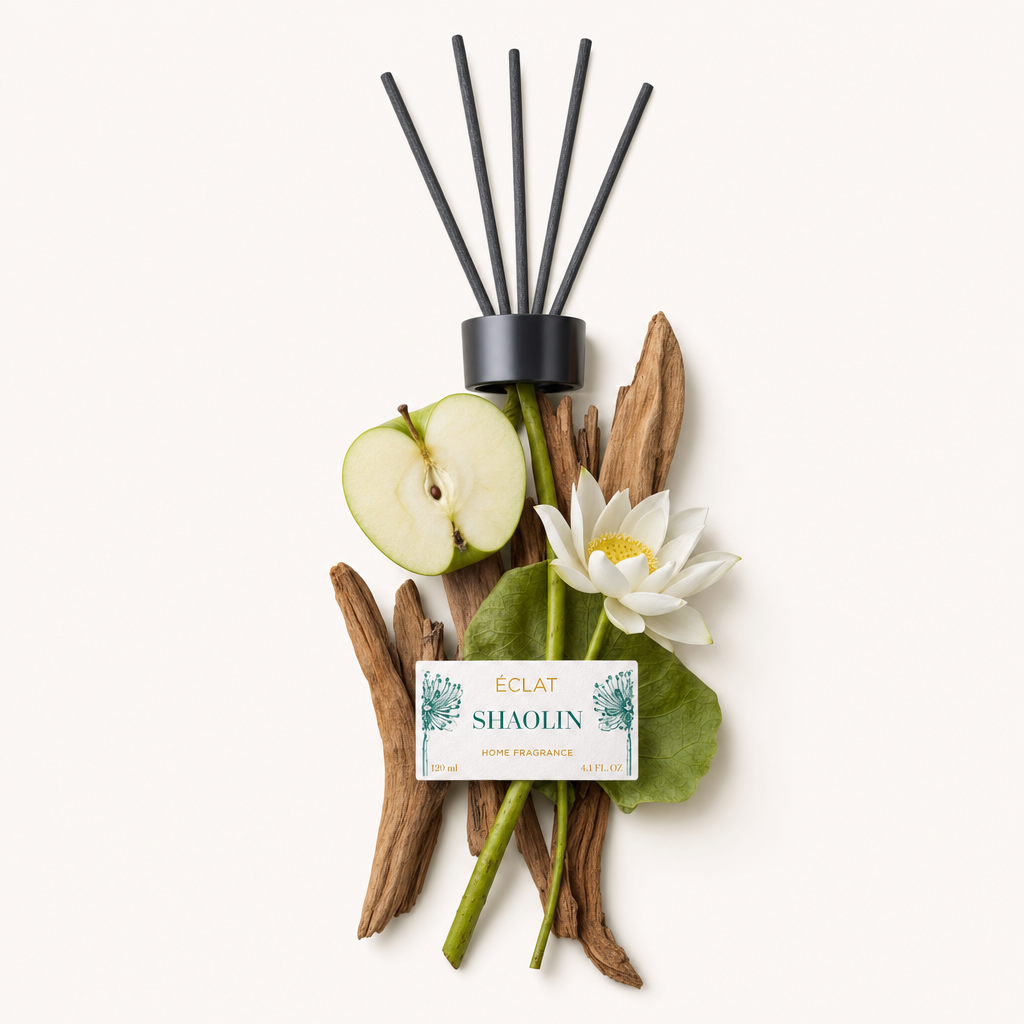 Un arrangement de bâtons de bois, une demi-pomme verte, une fleur de lotus blanche et des feuilles est magnifiquement disposé autour du capuchon noir avec l'étiquette de ÉCLAT Shaolin Room Fragrance Sticks.