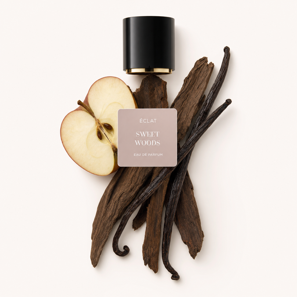 Un arrangement de tranches de pomme, de gousses de vanille et de bâtons de bois crée une composition naturelle sous l'étiquette ÉCLAT Sweet Woods et le bouchon noir d'origine.