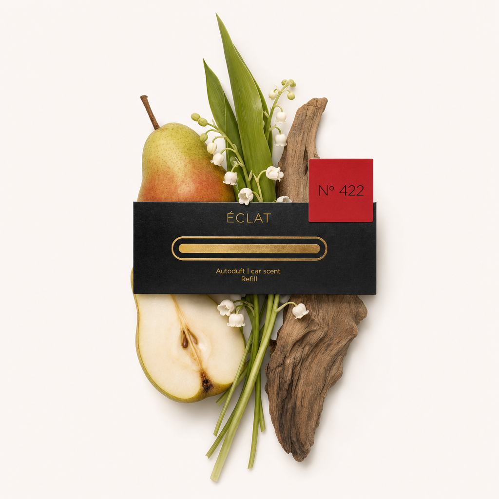 Een compositie van een gesneden peer, lelietje-van-dalen bloemen, groene bladeren en drijfhout, aangevuld met het zwarte ÉCLAT-dopje met rood label.