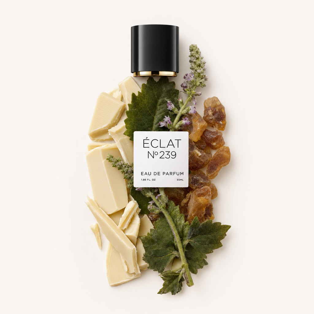Un arrangement de morceaux de chocolat blanc, de feuilles de patchouli fraîches et de résine, avec un capuchon noir portant l'étiquette ÉCLAT 239.