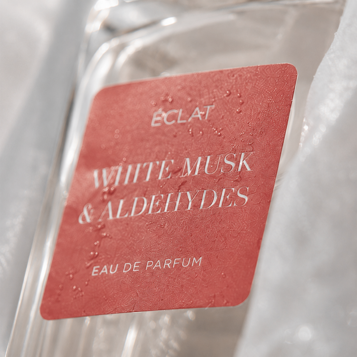 Close-up of the ÉCLAT White Musk & Aldehydes perfume bottle with a textured red label.