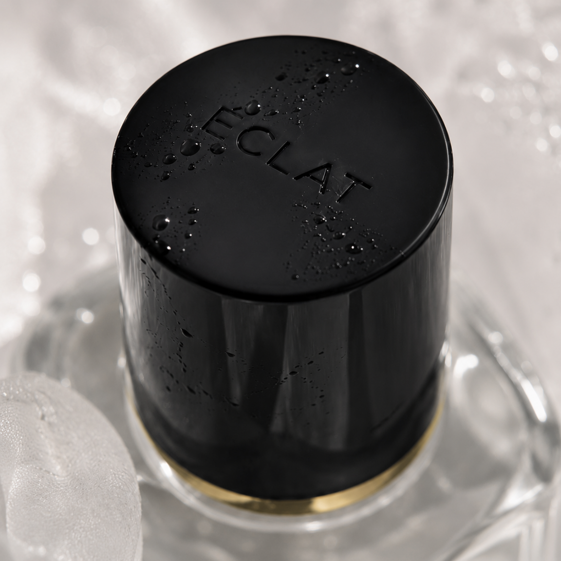 Faceted glass bottle with a black cap embossed with ÉCLAT, adorned with water droplets.