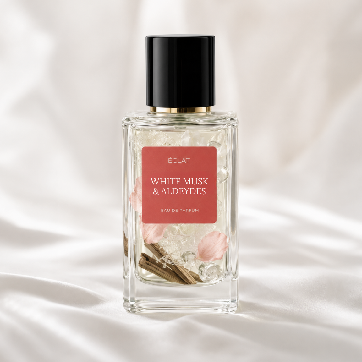 ÉCLAT White Musk & Aldehydes in a faceted glass bottle with a black cap and a red label on a soft, white fabric background.