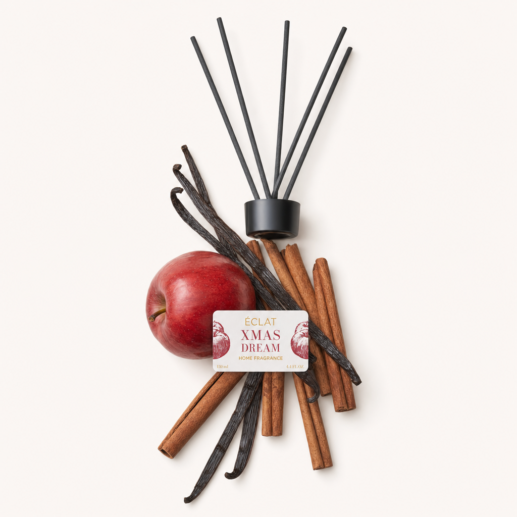 Ett arrangemang av ett rött äpple, kanelstänger och vaniljstänger för ÉCLAT Xmas Dream Room Fragrance Sticks, bredvid den ursprungliga svarta locket med etikett.